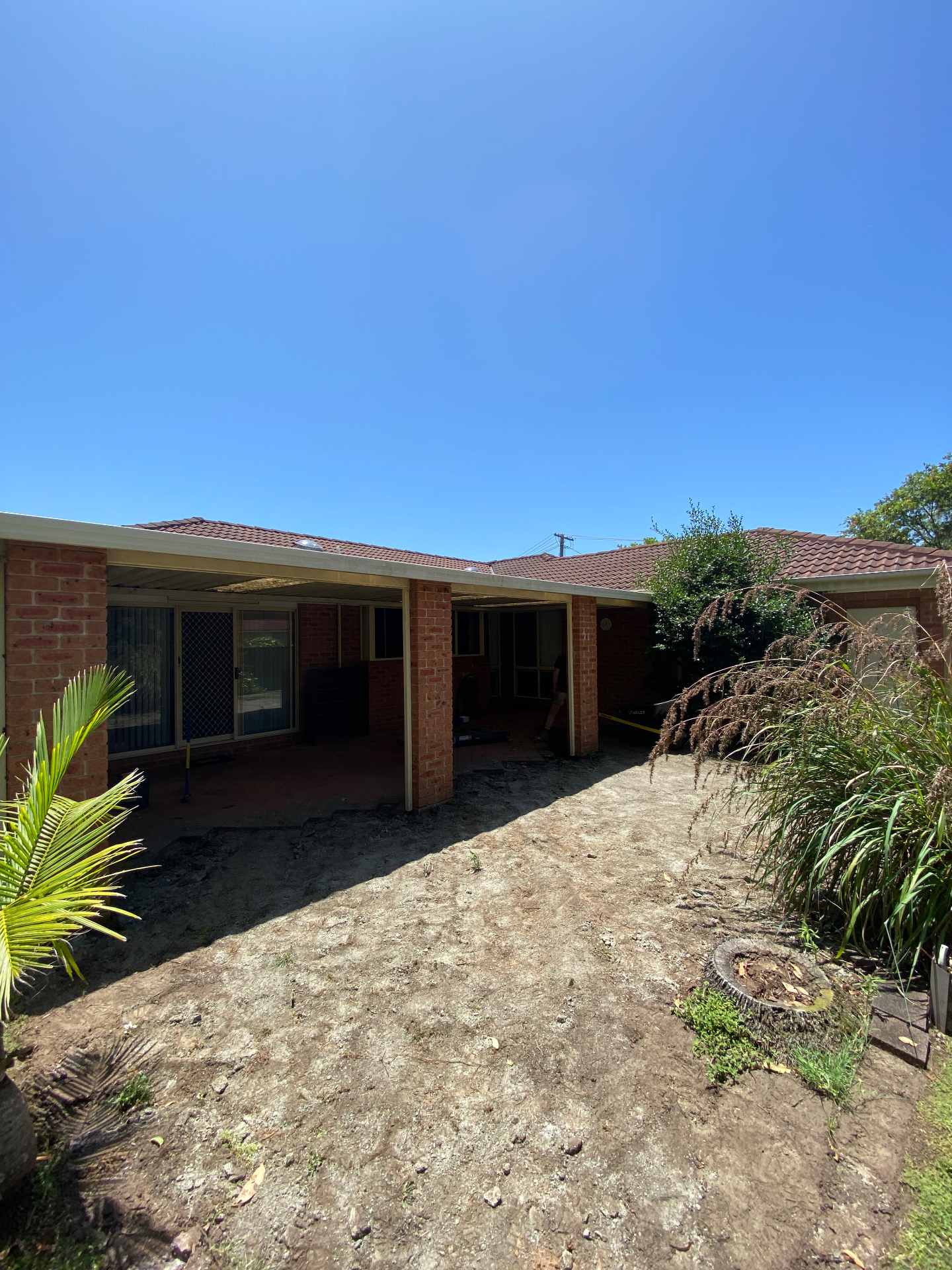 Before: bare dirt and stripped paving under an old pergola at the rear of a Chittaway Bay home