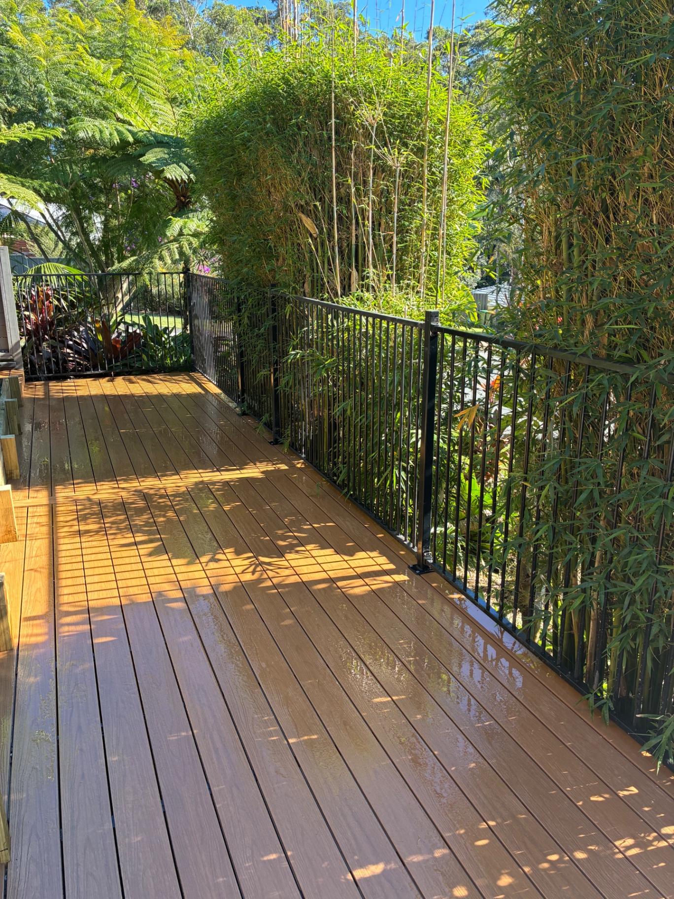 Composite deck walkway with black aluminium balustrade running alongside bamboo screening
